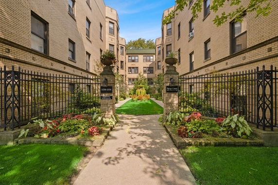 Front view of a brick apartment building with a gated entrance and landscaped path.