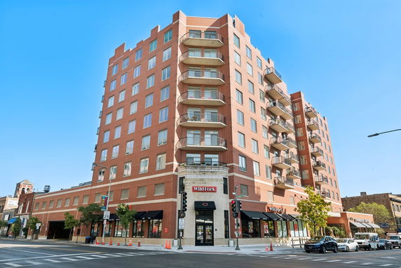 Front view of a multi-story brick building with balconies and ground floor retail space.