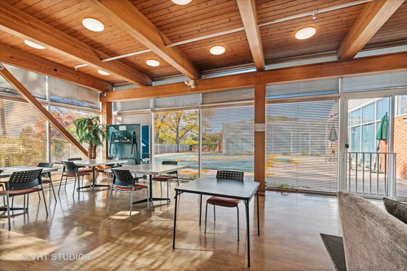 Indoor recreational area with tables and chairs, featuring large windows with blinds.