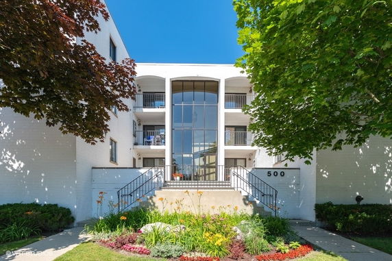 Front view of a multi-story building with a central glass facade and steps leading to the entrance.