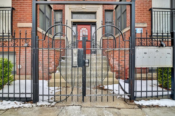 Front view of a brick building with a red door and gated entrance.
