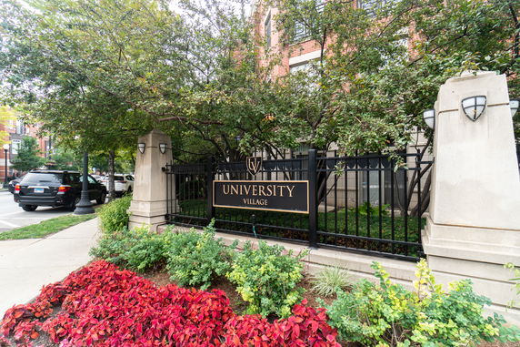 Front view of a building with a black fence and a sign reading 'University Village.'