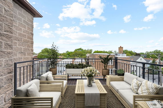 Rooftop patio with outdoor seating and plants, offering a panoramic view of surrounding buildings and trees.
