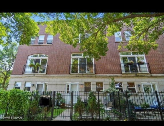 Front view of a multi-story brick building with balconies and fenced entryway.