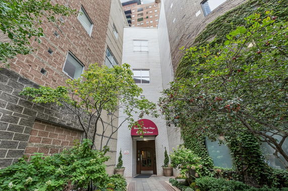 Front view of a multi-story building entrance with red awning and surrounding greenery.
