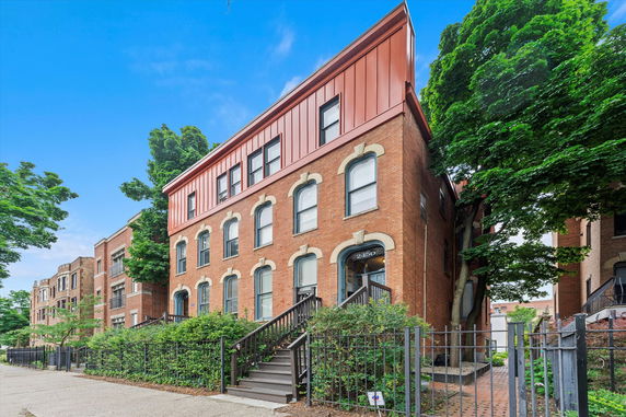 Front view of a three-story brick building with a modern metal-clad top floor and arched windows.
