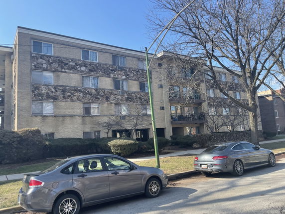 Front view of a multi-story residential building with balconies and parked cars in front.