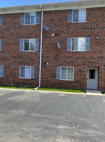 Front view of a brick apartment building with multiple windows and satellite dishes.