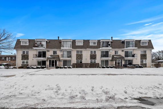 Front view of a three-story residential building with multiple balconies and a pitched roof.