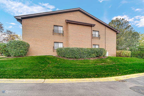 Side view of a two-story brick building with windows and shrubs.