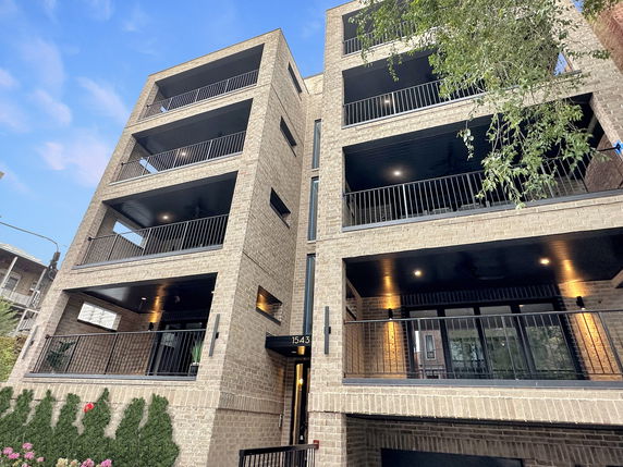 Front view of a multi-story brick building with balconies and black railings.