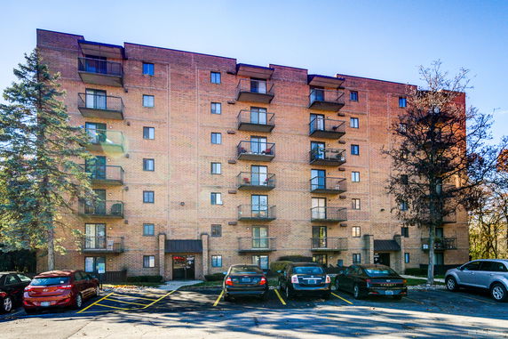 Front view of a multi-story apartment building with balconies and parking space.