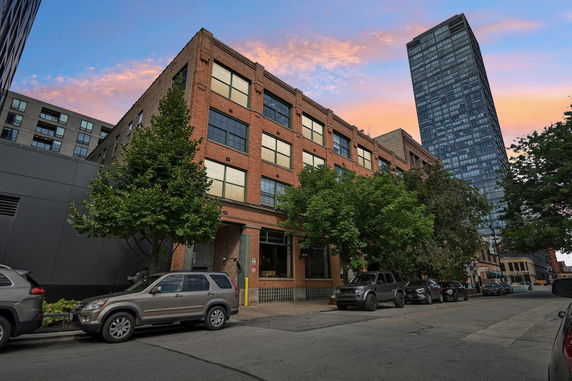 Front view of a four-story brick building with large windows and a modern high-rise building visible in the background.