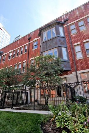 Front view of a multi-story brick building with bay windows and metal fencing.