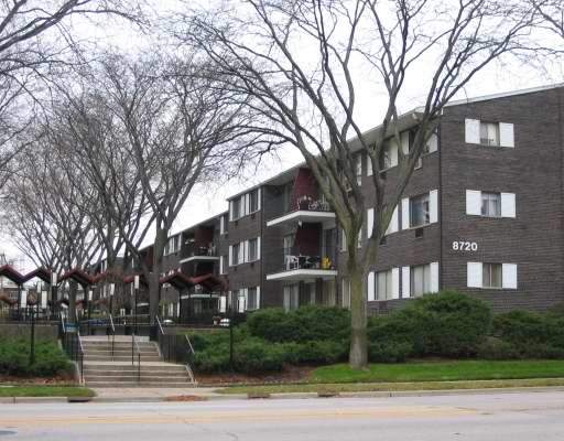 Front view of a multi-story apartment building with exterior balconies and exposed brickwork.