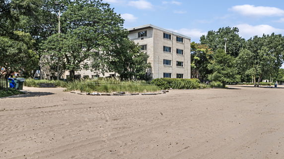 Front view of a multi-story building surrounded by trees and sandy area.