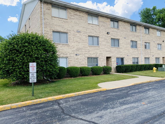 Front view of a three-story brick building with multiple windows and a sidewalk in front.