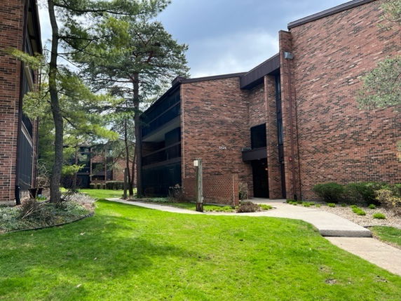 Front view of a brick multi-story apartment building with balconies and surrounding greenery.