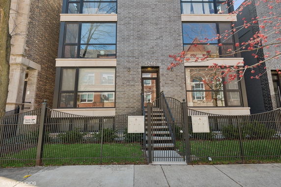 Front view of a multi-story modern building with large windows and a gated entrance.