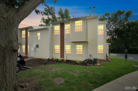 Front view of a multi-story building with illuminated windows and beige siding.