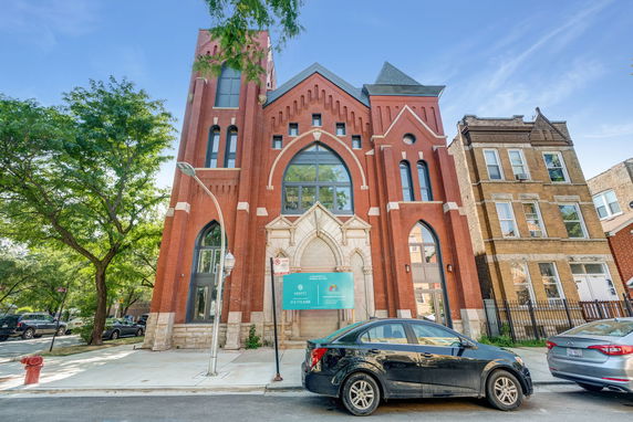 Front view of a red brick building with arched windows and a pointed roof.