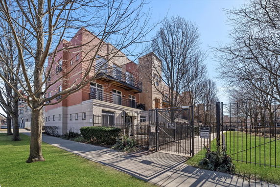 Front view of a multi-story brick building with balconies and gated entrance.