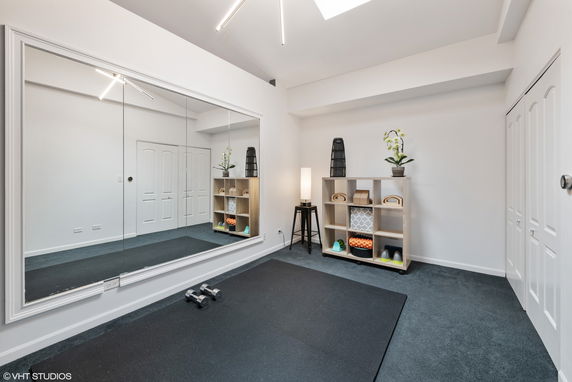 Indoor gym area with a large mirror, workout mat, and shelf with fitness equipment.
