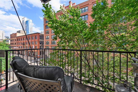 View from a balcony overlooking urban buildings with trees and seating area.