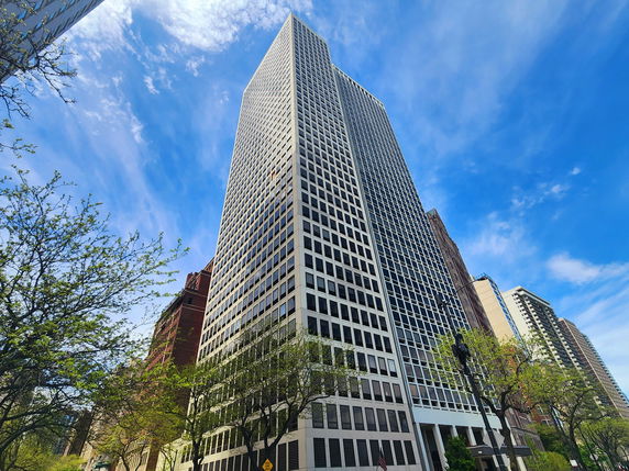 View of a tall skyscraper with a grid of windows against a blue sky.