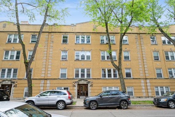 Front view of a multi-story brick building with multiple windows and parked cars in front.