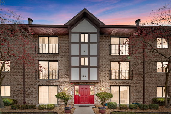 Front view of a three-story brick building with red door and multiple balconies.