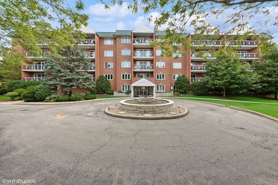 Front view of a multi-story brick apartment building with balconies and a circular driveway.