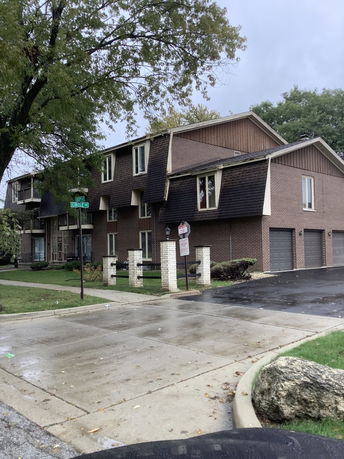 Side view of a multi-story residential building with a sloped roof and garages.