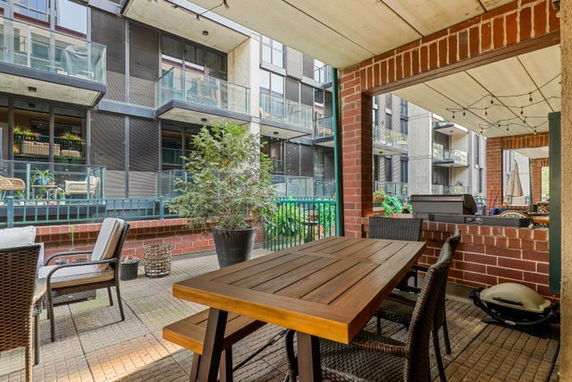 Outdoor seating area with wooden table, chairs, and potted plants, overlooking a residential building with balconies.