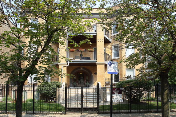 Front view of a multi-story building with balconies and a fenced entrance.