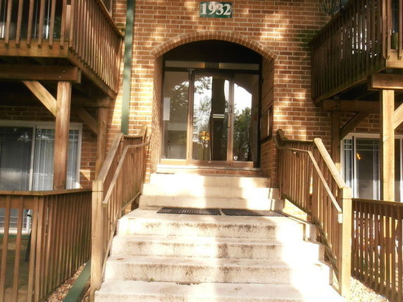 Front view of a brick building entrance with stairs and wooden railings.