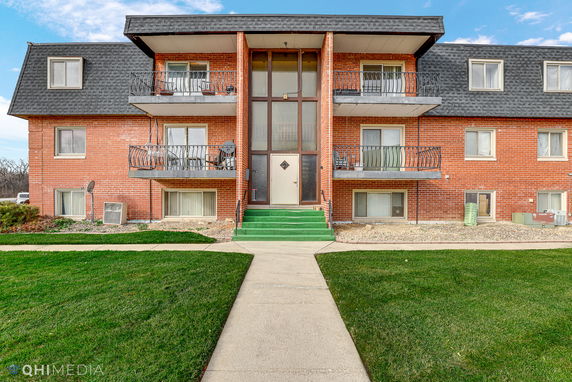 Front view of a three-story brick apartment building with balconies and a central entrance.