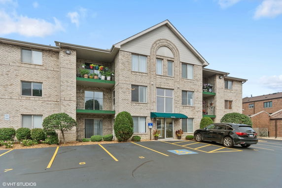 Front view of a three-story brick apartment building with balconies and a parking area.