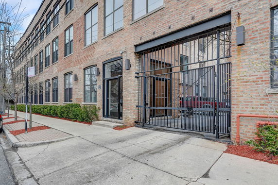Front view of a multi-story brick building with large windows and a gated entrance.