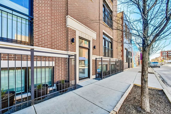 Front view of a brick multi-story building with metal railings and a tree-lined sidewalk.