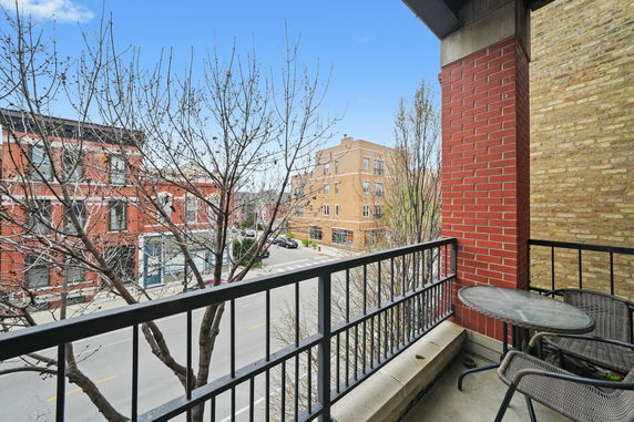 View from a balcony overlooking a city street with nearby buildings and trees.