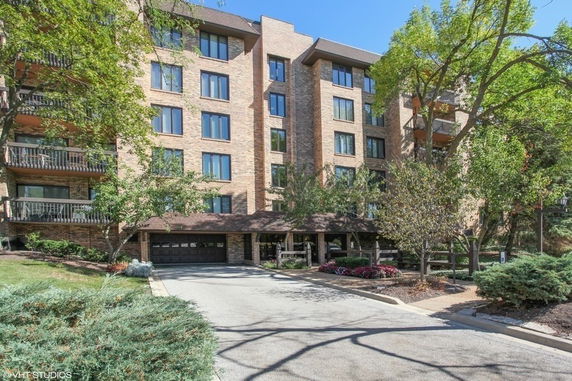 Front view of a multi-story brick building with balconies and surrounding trees.