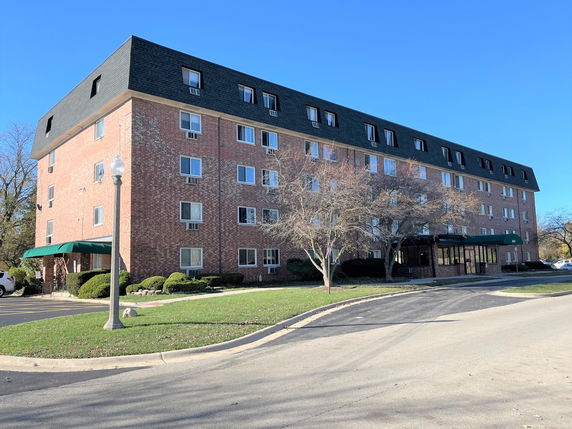 Front view of a multi-story brick apartment building with multiple windows and a black roof.