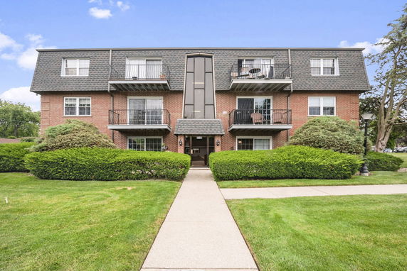 Front view of a three-story brick apartment building with balconies.