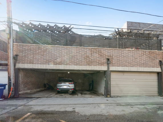 Outdoor covered parking structure with a car parked under a brick building.