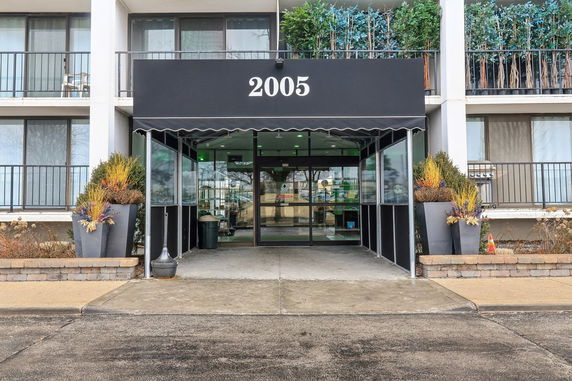 Front view of a building entrance with black canopy and potted plants.