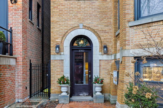 Front view of a brick townhouse entryway with a decorative arch and plants.