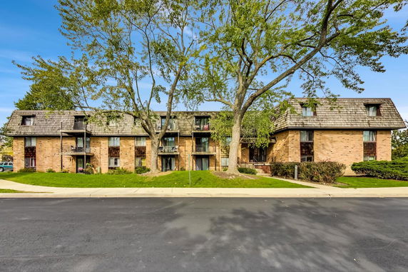 Front view of a multi-story brick apartment building with a sloped roof and balconies.