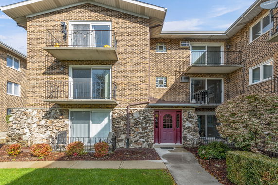Front view of a multi-story brick apartment building with balconies and a red door entrance.