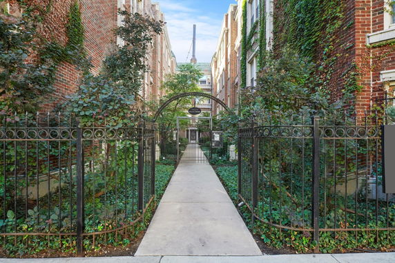 Front view of a brick apartment building with an arched gateway and greenery.